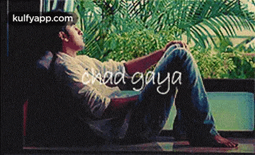 a man is sitting on the floor in front of a window with the words chad gaya written on it .