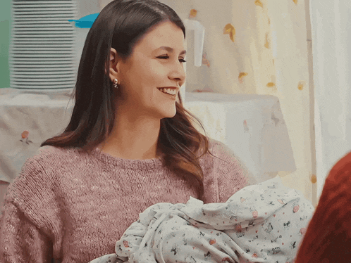 a woman in a pink sweater is holding a baby in a blanket
