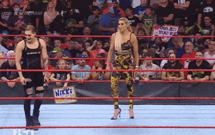 a woman holding a sign that says nikki stands in a wrestling ring