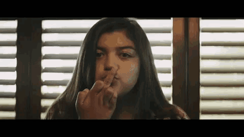 a young girl is sitting in front of a window with blinds and eating a candy bar .
