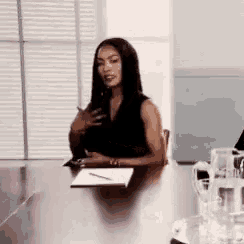 a woman is sitting at a table in a conference room with a notebook and pen .
