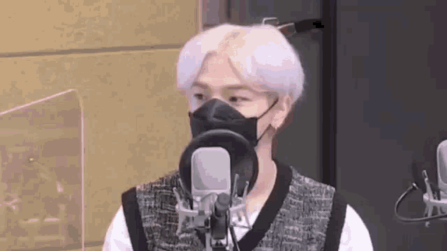 a man wearing a mask is standing in front of a microphone in a studio .