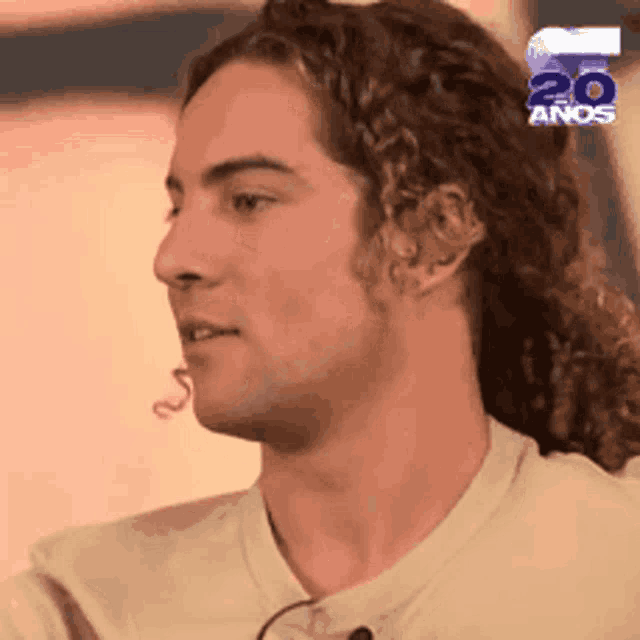 a man with long curly hair is wearing a white shirt with the number 20 anos on it