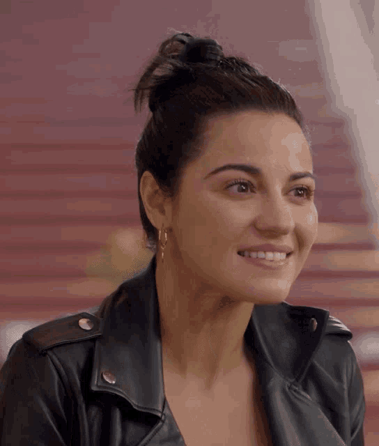 a woman wearing a leather jacket and earrings smiles