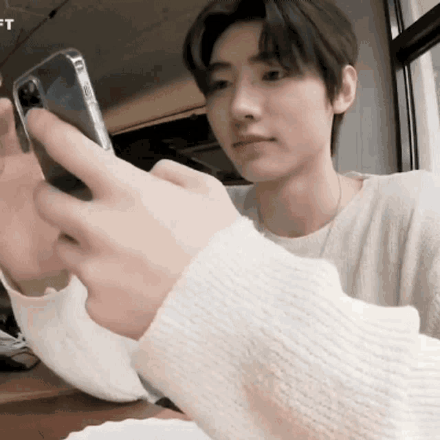 a young man in a white sweater is looking at his cell phone