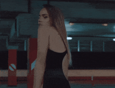 a woman in a black swimsuit is standing in a dark room with her hair blowing in the wind .