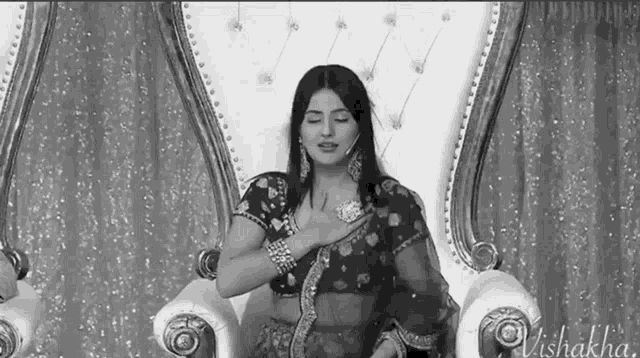 a woman in a saree sits in a chair with the name vishakha on the bottom right