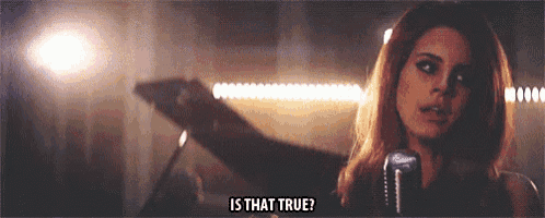 a woman is singing into a microphone in a dark room and asking is that true .