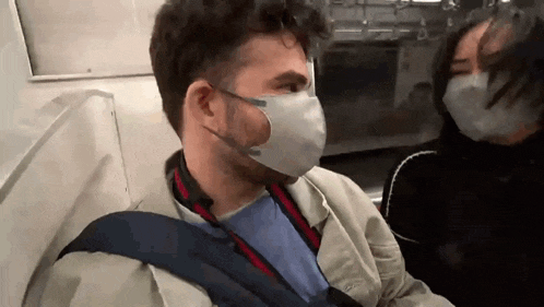 a man and a woman wearing face masks are sitting on a train .