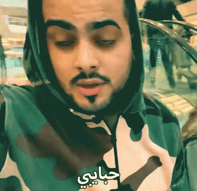 a man wearing a camouflage hoodie has arabic writing on his shirt