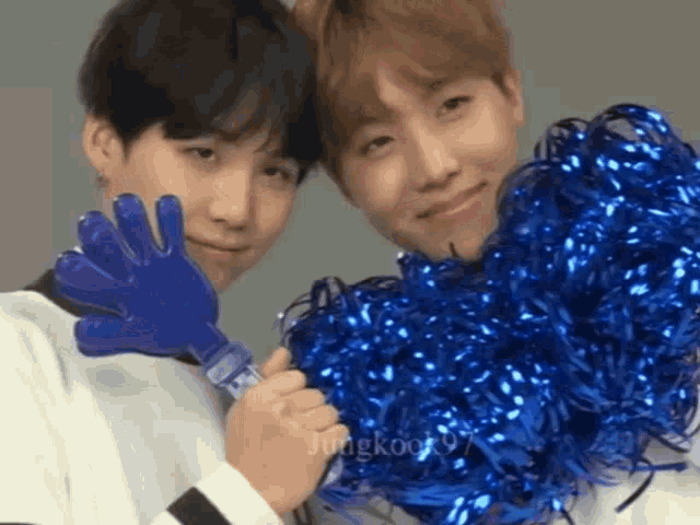 a couple of boys are holding blue pom poms and gloves .