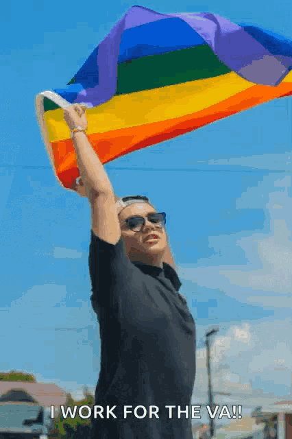 a man is holding a rainbow flag over his head and says i work for the va !