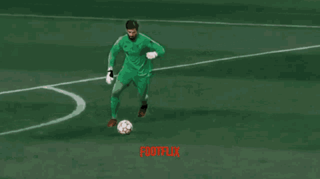 a soccer goalie in green kicks a soccer ball while a player in red tries to block him
