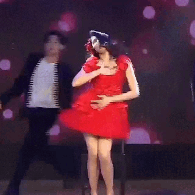 a woman in a red dress is dancing with a man in a black jacket behind her