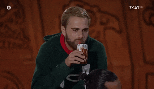 a man in a green sweatshirt is drinking from a cup with a straw and the letters kat hd on the bottom left