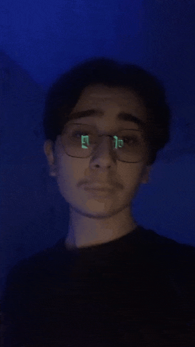 a young man wearing glasses and a black shirt looks at the camera