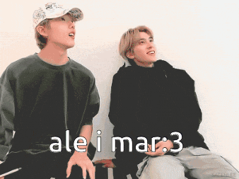 two young men are sitting next to each other and one of them is wearing a baseball cap and the other is wearing a black sweater
