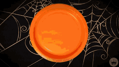 an orange paper plate is sitting on a table with a spider web behind it