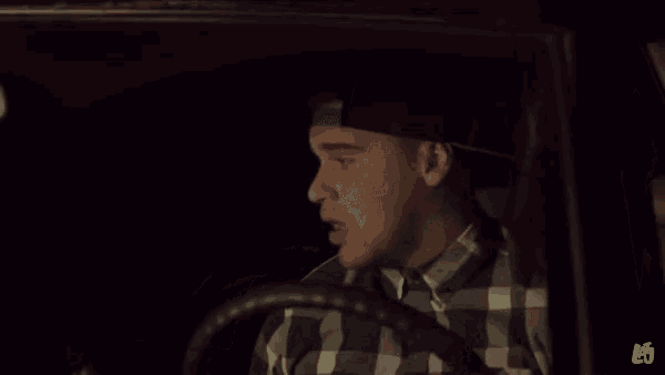 a man in a plaid shirt is smiling while driving a car at night