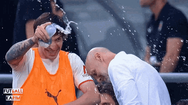 a man in an orange vest with a puma logo pours water on another man