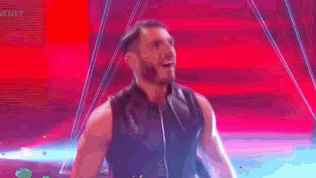 a man in a black leather vest is standing in front of a pink background .