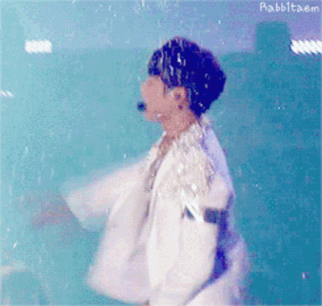 a man in a white jacket is dancing in front of a blue background with rabbittaem written on the bottom