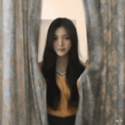 a woman with long black hair is peeking through a window curtain