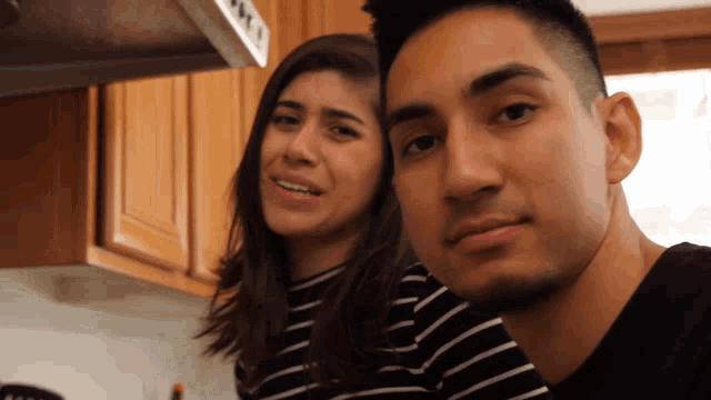 a man and a woman are posing for a picture in a kitchen and the man is wearing a black shirt