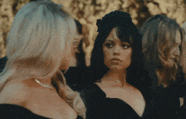 a woman in a black dress with a veil on her head stands next to two other women