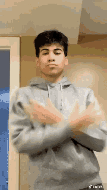 a young man in a gray hoodie is standing in front of a door making a funny face .