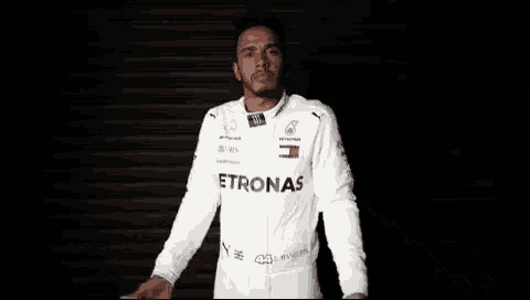 a man wearing a white petronas racing suit is standing with his arms outstretched .