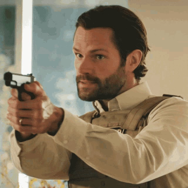 a man with a beard is pointing a gun with the letter p on his vest