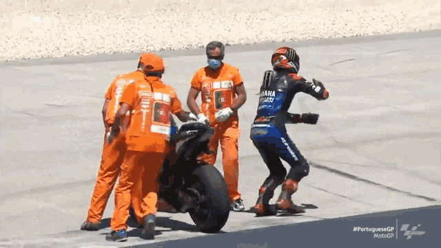 a motorcycle racer wearing a monster helmet is being helped by a group of men