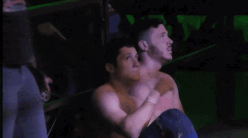 two men are wrestling in a dark room and one is wearing blue shorts