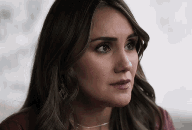 a close up of a woman 's face with a necklace that has the letter e on it