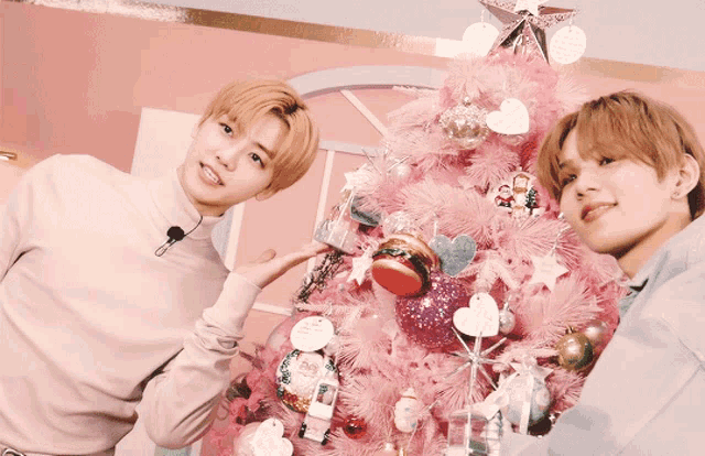 two young men standing next to a pink christmas tree with hearts on it