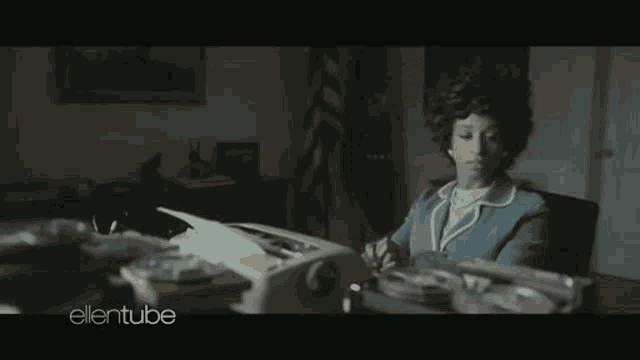 a woman in a blue suit sits at a desk with a typewriter and the words ellentube on the bottom