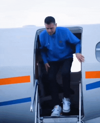 a man in a blue sweater is walking out of a plane