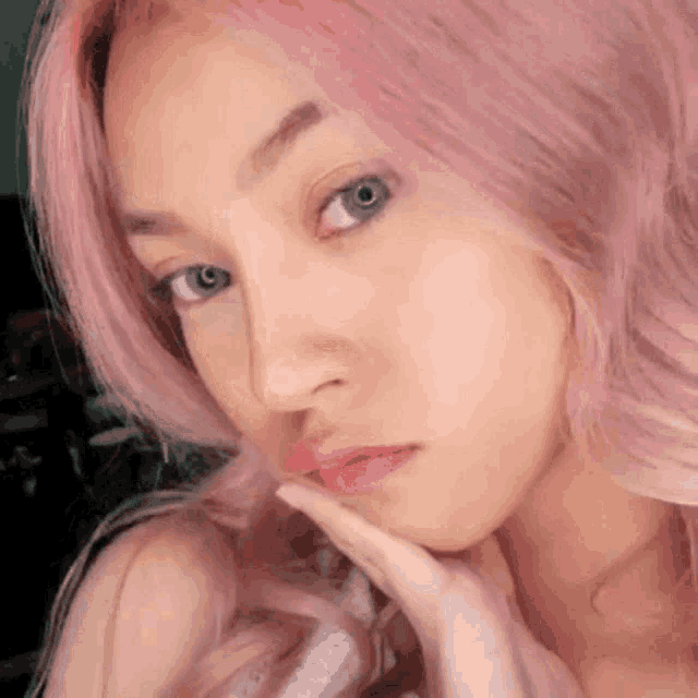 a close up of a woman 's face with pink hair and blue eyes