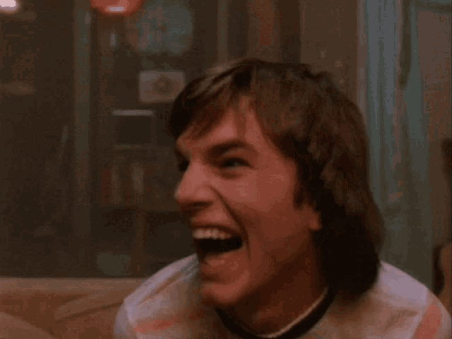 a young man sitting on a couch laughing with his mouth open