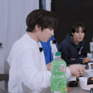 a man is sitting at a table holding a green bottle of soda .
