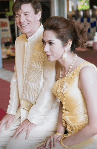 a man in a white suit sits next to a woman in a gold dress