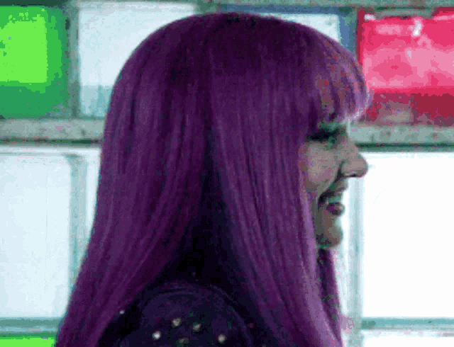 a woman with purple hair is smiling and looking to the side .