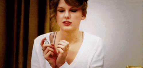 a woman in a white shirt is holding a bottle of lipstick in her hands .