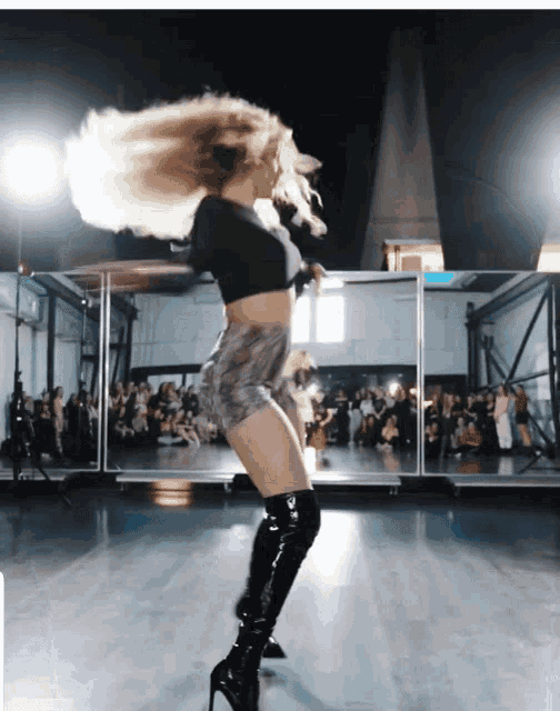 a woman in a black top and black boots is dancing in front of a crowd