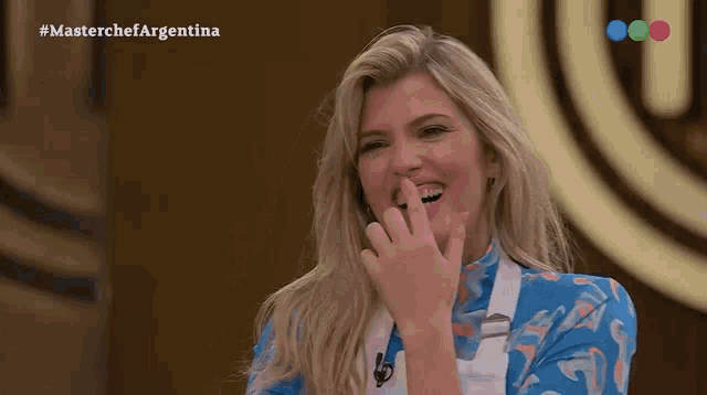 a woman is laughing in front of a masterchef argentina sign