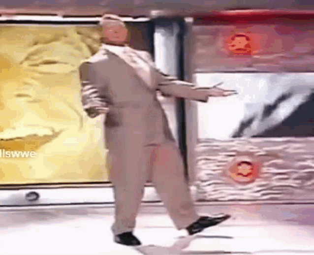 a man in a suit is dancing on a stage in front of a wall with a picture of a man on it .