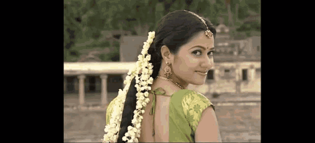 a woman with flowers in her hair is wearing a green blouse and looking at the camera .