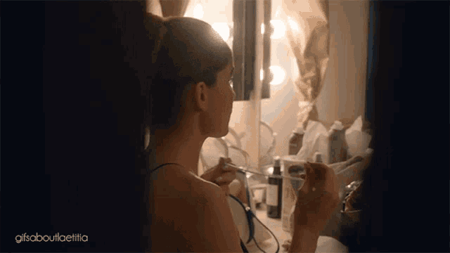 a woman is applying makeup in front of a mirror with a gif about it written on the bottom