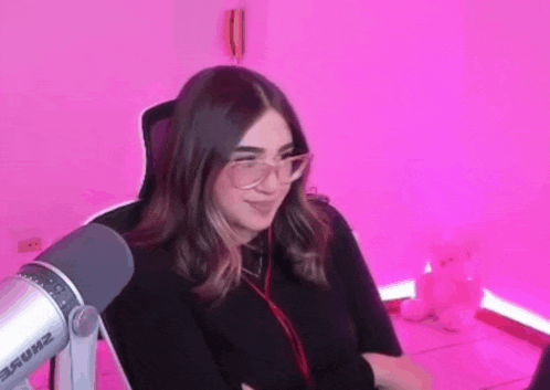 a girl wearing glasses is sitting in front of a microphone in a pink room .